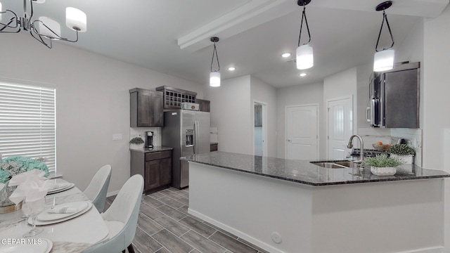 kitchen featuring appliances with stainless steel finishes, hanging light fixtures, dark stone counters, sink, and dark brown cabinets