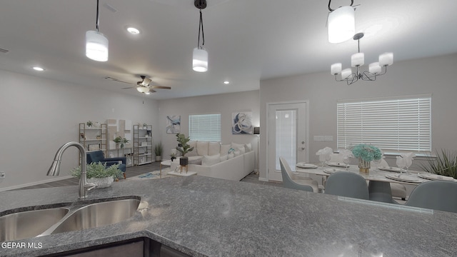 kitchen featuring decorative light fixtures, ceiling fan with notable chandelier, sink, and dark stone counters
