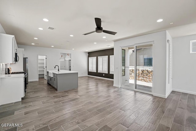 kitchen featuring white cabinets, decorative light fixtures, stainless steel appliances, a kitchen island with sink, and ceiling fan