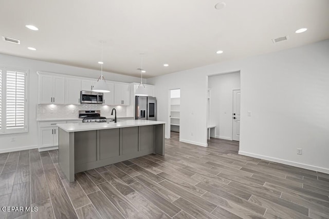 kitchen featuring decorative light fixtures, white cabinetry, stainless steel appliances, and a kitchen island with sink