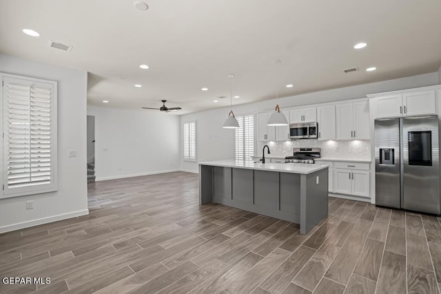 kitchen with decorative light fixtures, white cabinets, a center island with sink, light hardwood / wood-style floors, and stainless steel appliances