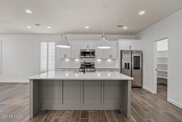 kitchen with stainless steel appliances, white cabinetry, a kitchen island with sink, and decorative light fixtures