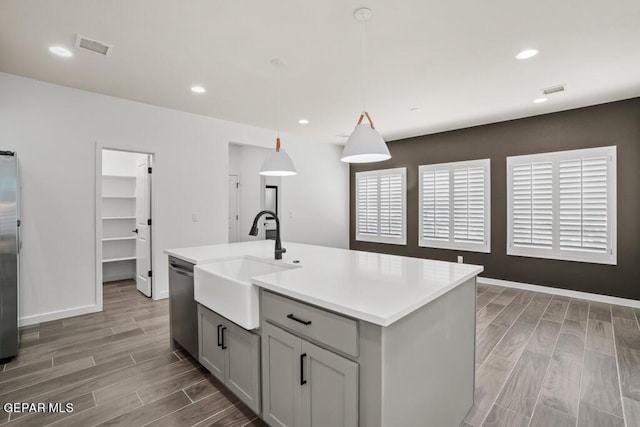 kitchen with appliances with stainless steel finishes, sink, hanging light fixtures, gray cabinets, and a center island with sink