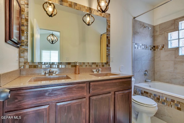 full bathroom with double sink vanity, toilet, tiled shower / bath combo, and an inviting chandelier