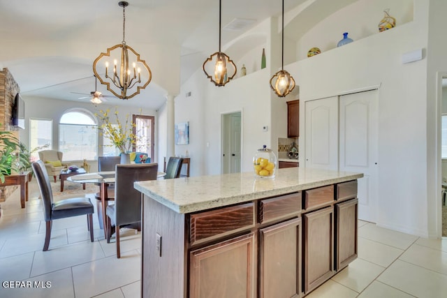 kitchen with pendant lighting, a kitchen island, light tile floors, and ceiling fan with notable chandelier