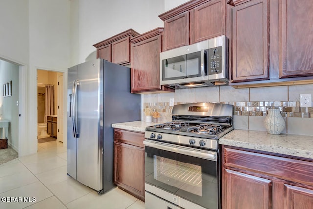 kitchen with light tile floors, light stone countertops, a towering ceiling, appliances with stainless steel finishes, and backsplash