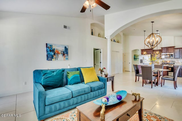 tiled living room featuring ornate columns, high vaulted ceiling, and ceiling fan with notable chandelier