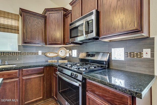 kitchen with dark stone counters, backsplash, sink, and stainless steel appliances