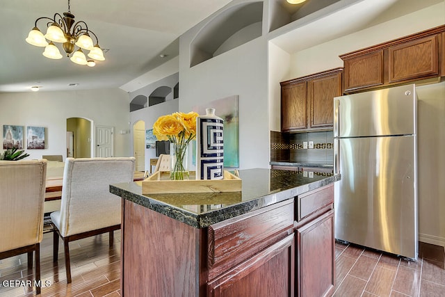 kitchen featuring an inviting chandelier, stainless steel appliances, a center island, dark stone counters, and tasteful backsplash