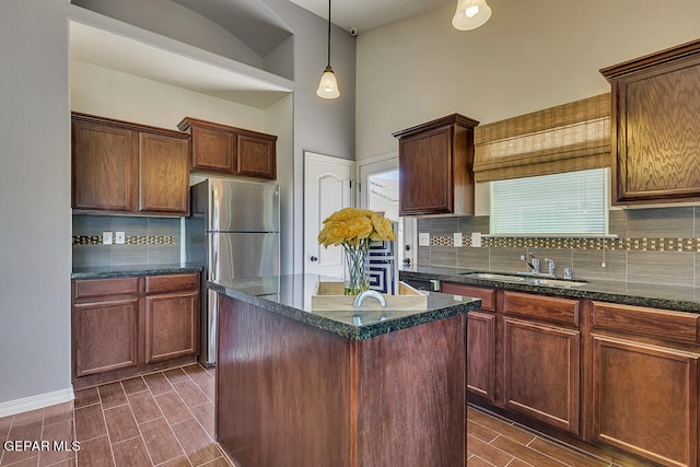 kitchen with pendant lighting, tasteful backsplash, a kitchen island, dark stone countertops, and sink