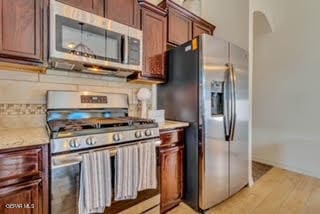 kitchen with light wood-type flooring, light stone countertops, and appliances with stainless steel finishes