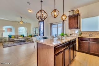 kitchen with a center island, ceiling fan with notable chandelier, light hardwood / wood-style flooring, hanging light fixtures, and light stone counters