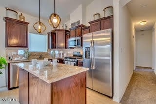 kitchen with pendant lighting, a kitchen island, appliances with stainless steel finishes, and light stone countertops