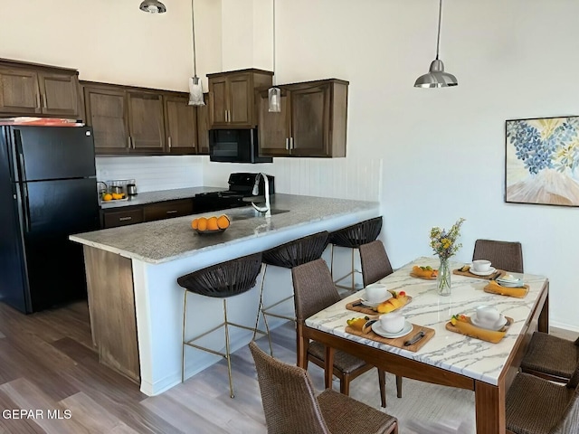 kitchen featuring black appliances, wood finished floors, and dark brown cabinets
