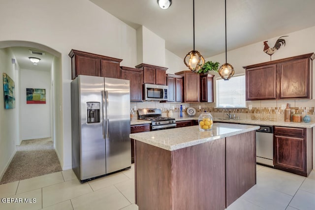 kitchen featuring tasteful backsplash, a kitchen island, stainless steel appliances, light tile floors, and decorative light fixtures