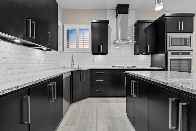 kitchen featuring wall chimney exhaust hood, light hardwood / wood-style floors, stainless steel appliances, and tasteful backsplash