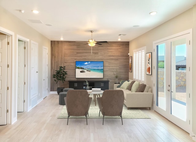 living room with french doors, wooden walls, ceiling fan, and light wood-type flooring