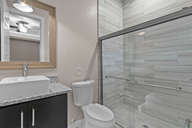 bathroom with ceiling fan, toilet, a shower with shower door, and vanity with extensive cabinet space