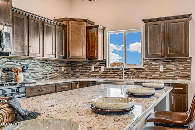 kitchen with tasteful backsplash, a kitchen bar, sink, and light stone countertops