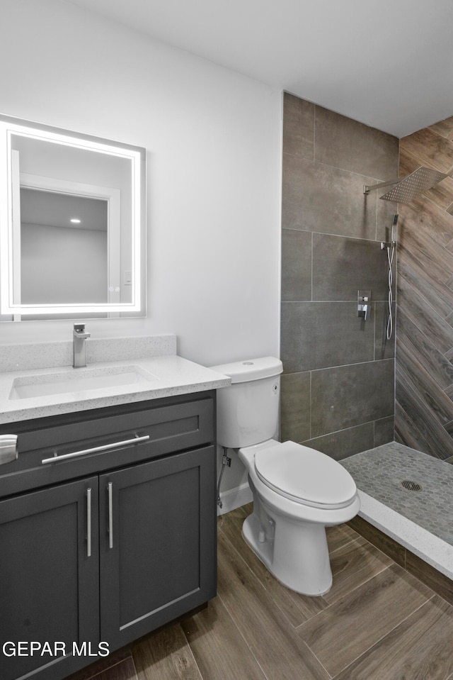 bathroom with wood-type flooring, toilet, vanity, and tiled shower