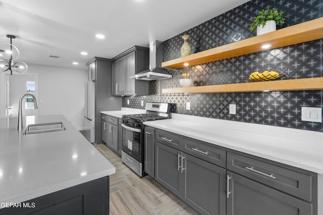 kitchen featuring an inviting chandelier, wall chimney range hood, backsplash, sink, and stainless steel gas range