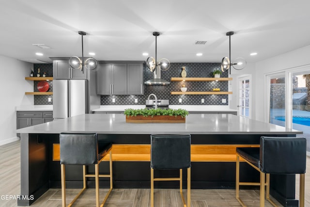 interior space featuring backsplash, gray cabinetry, a center island with sink, and stainless steel refrigerator