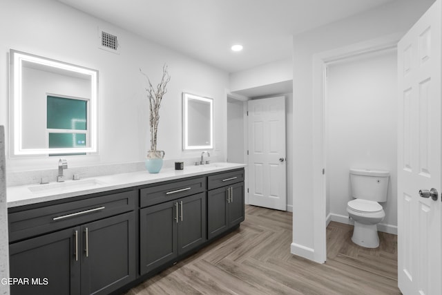 bathroom with parquet flooring, toilet, and dual bowl vanity