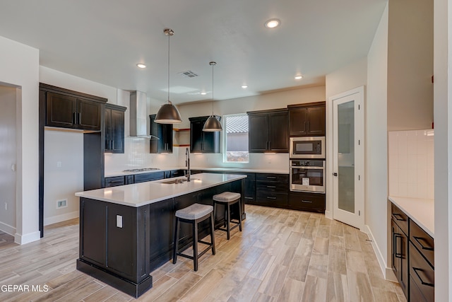 kitchen with visible vents, a sink, decorative backsplash, appliances with stainless steel finishes, and wall chimney range hood