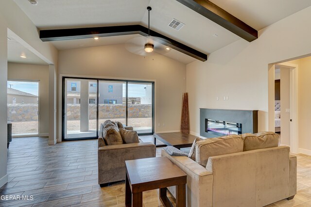 living room featuring visible vents, light wood-style flooring, lofted ceiling with beams, a glass covered fireplace, and baseboards