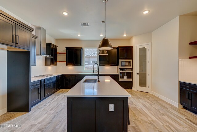 kitchen featuring visible vents, light wood finished floors, a sink, stainless steel appliances, and wall chimney range hood