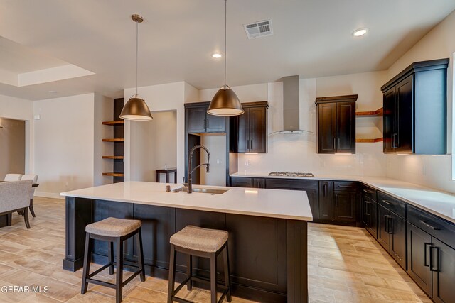 kitchen with visible vents, open shelves, wall chimney range hood, stainless steel gas stovetop, and a sink