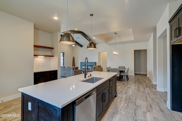 kitchen featuring light wood finished floors, open floor plan, light countertops, stainless steel dishwasher, and a sink