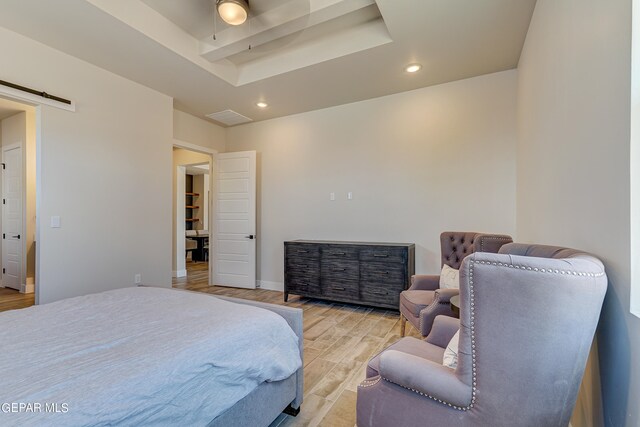 bedroom with baseboards, a tray ceiling, recessed lighting, light wood-style floors, and a barn door