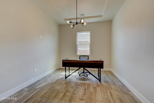 office space with a tray ceiling, baseboards, visible vents, and light wood-type flooring