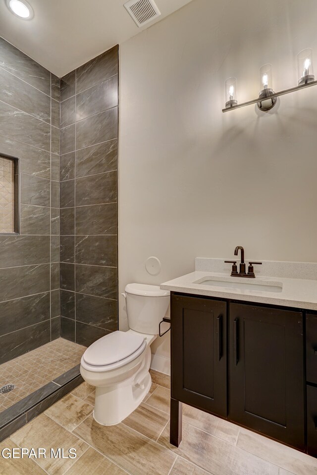 full bathroom featuring a tile shower, visible vents, toilet, and vanity