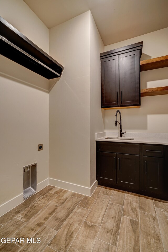 clothes washing area featuring cabinet space, baseboards, wood tiled floor, and a sink