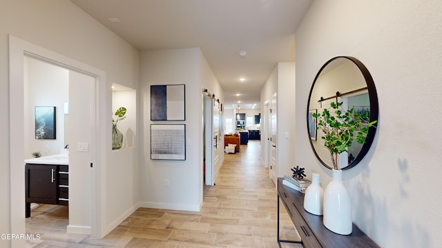 hallway featuring light wood-type flooring, recessed lighting, baseboards, and a barn door