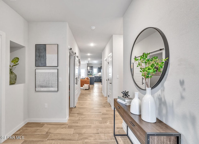 corridor featuring recessed lighting, baseboards, light wood finished floors, and a barn door