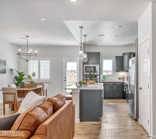 kitchen with visible vents, light countertops, freestanding refrigerator, a center island, and decorative light fixtures