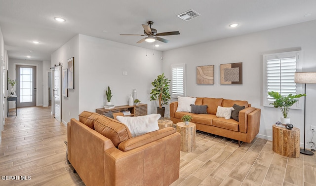 living area with ceiling fan, light wood finished floors, visible vents, and a healthy amount of sunlight