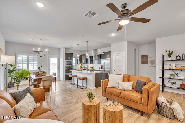 living room featuring light wood-type flooring, recessed lighting, visible vents, and ceiling fan with notable chandelier