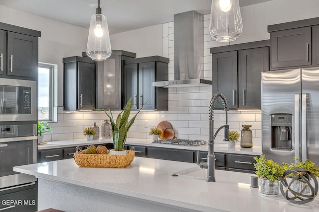 kitchen featuring stainless steel appliances, tasteful backsplash, pendant lighting, and wall chimney range hood