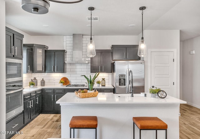 kitchen featuring wood finish floors, light countertops, appliances with stainless steel finishes, a kitchen island, and wall chimney exhaust hood