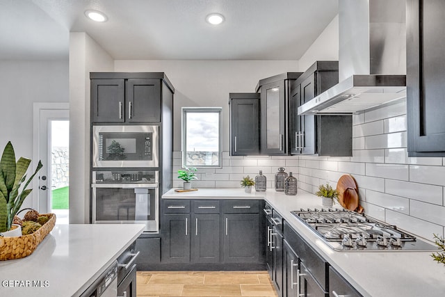 kitchen with wall chimney exhaust hood, stainless steel appliances, and backsplash