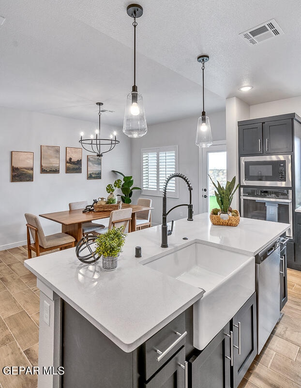 kitchen featuring sink, a kitchen island with sink, stainless steel appliances, a textured ceiling, and decorative light fixtures