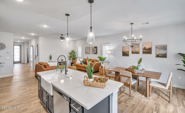 kitchen with sink, hanging light fixtures, dishwasher, a kitchen island with sink, and ceiling fan with notable chandelier