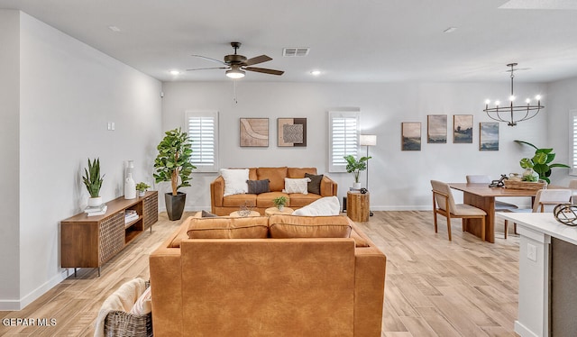 living room with light wood-style flooring, recessed lighting, ceiling fan with notable chandelier, visible vents, and baseboards