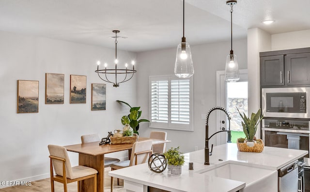 kitchen featuring decorative light fixtures, stainless steel appliances, light countertops, a kitchen island with sink, and a sink