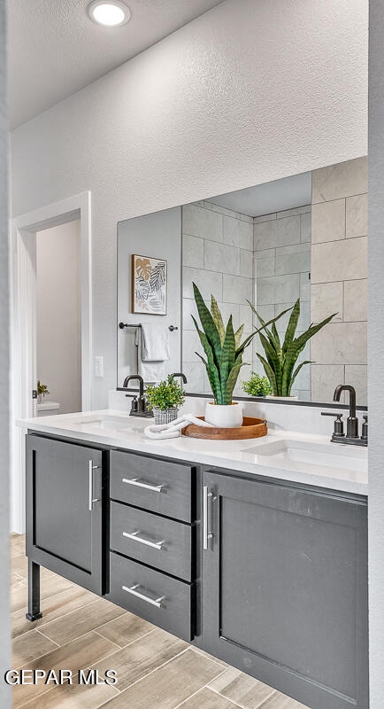 full bath with wood finish floors, a sink, a textured ceiling, and double vanity