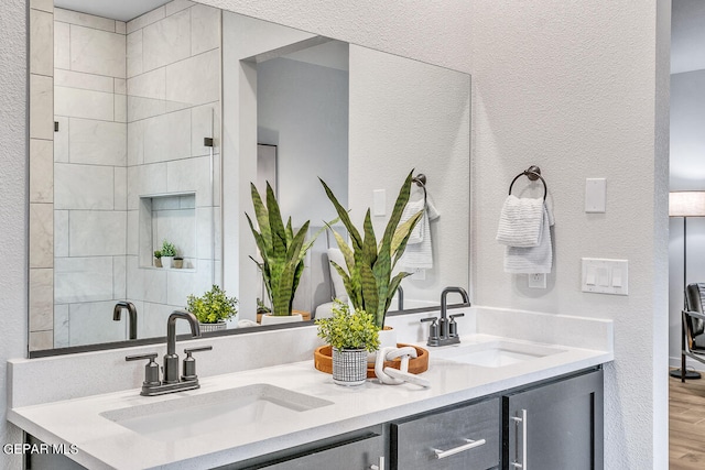 bathroom with a textured wall, wood finished floors, a sink, and double vanity